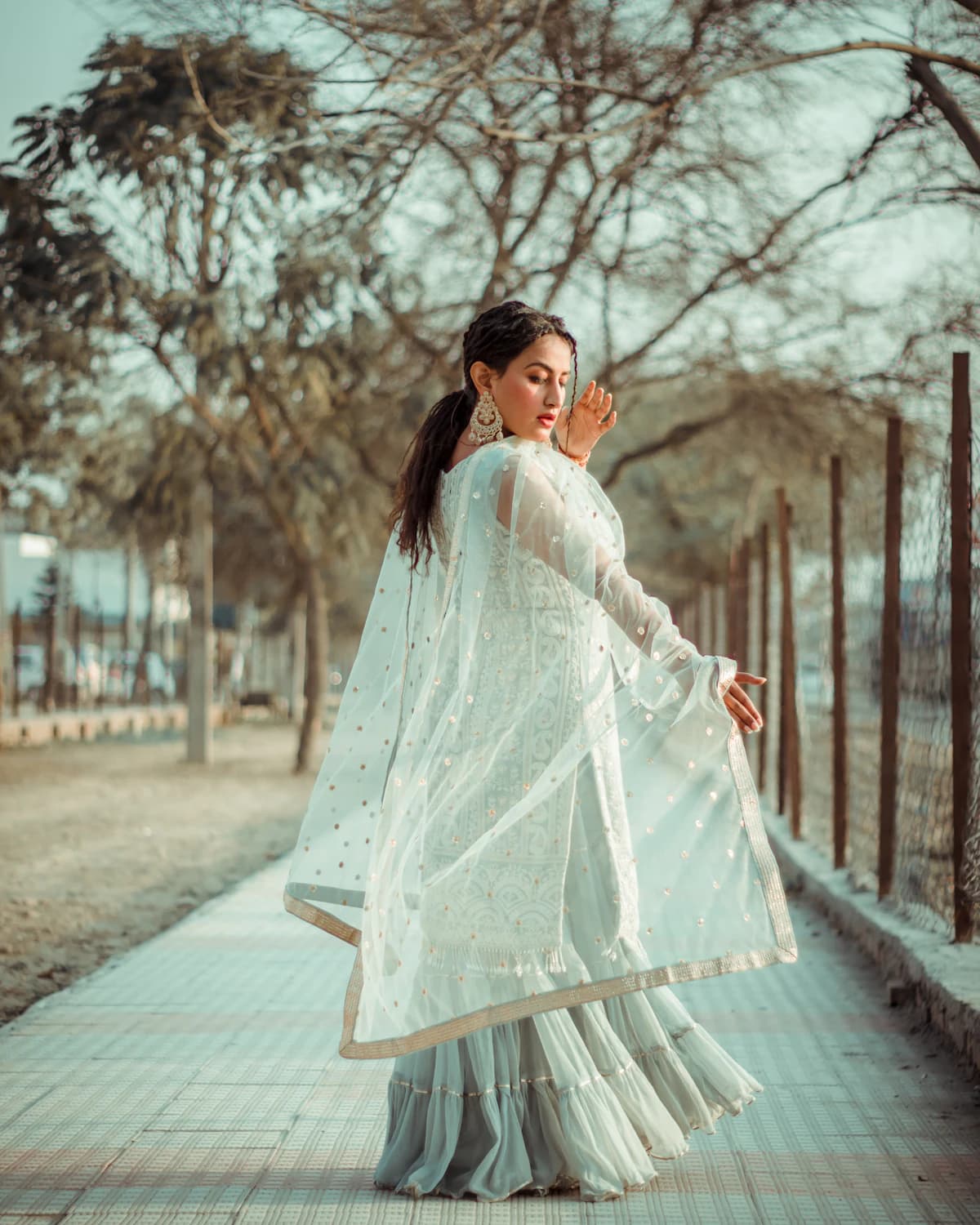 Woman in a pale lehenga walking on a tree-lined path